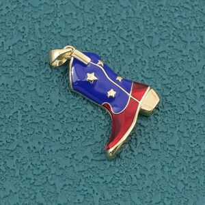 May include: A gold-toned metal pendant shaped like a cowboy boot, featuring blue enamel on the upper section with small gold stars and red enamel on the lower foot area. The pendant includes a small gold loop at the top for attachment to a chain.