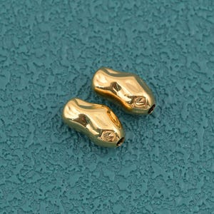 May include: Two small, gold-colored beads with an irregular, organic, and slightly elongated shape. Each bead features a smooth, reflective metallic surface with subtle indentations and curves, creating a polished appearance for jewelry making.