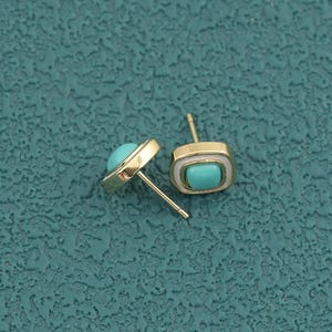 May include: A pair of gold-tone stud earrings featuring a square-shaped frame with rounded corners. Each earring contains a smooth, bright turquoise-colored inlay centered within the metal border, complete with a standard post backing.