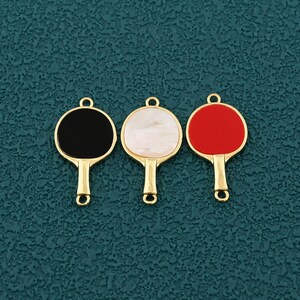 Pode incluir: Tr&ecirc;s pingentes dourados em forma de raquete de pingue-pongue. Uma raquete tem uma face preta, outra uma face branca perolada e a terceira uma face vermelha. Cada pingente tem uma argola na parte superior para fixa&ccedil;&atilde;o.