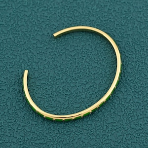 May include: Gold-tone open cuff bracelet with a green enamel inlay featuring a star pattern. The bracelet has a simple, elegant design and is displayed on a teal-colored surface. A stylish piece of jewelry.