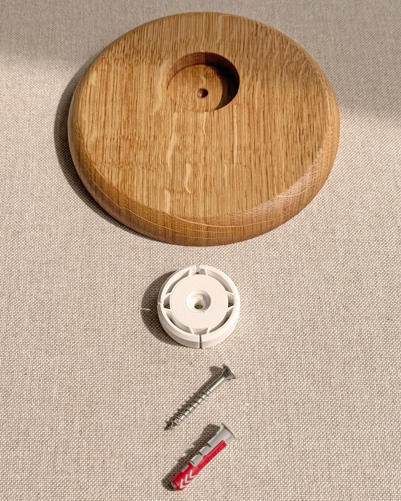May include: A wooden, circular object with a central hole, accompanied by a white plastic piece, a silver screw, and a red and white wall anchor. The wood has a natural grain pattern.