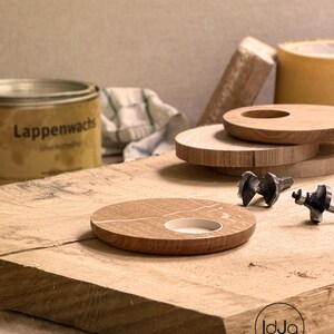 May include: A wooden candle holder with a white inlay and a circular opening. Several other wooden discs and tools are arranged on a wooden surface. A can of Lappenwachs is visible in the background.