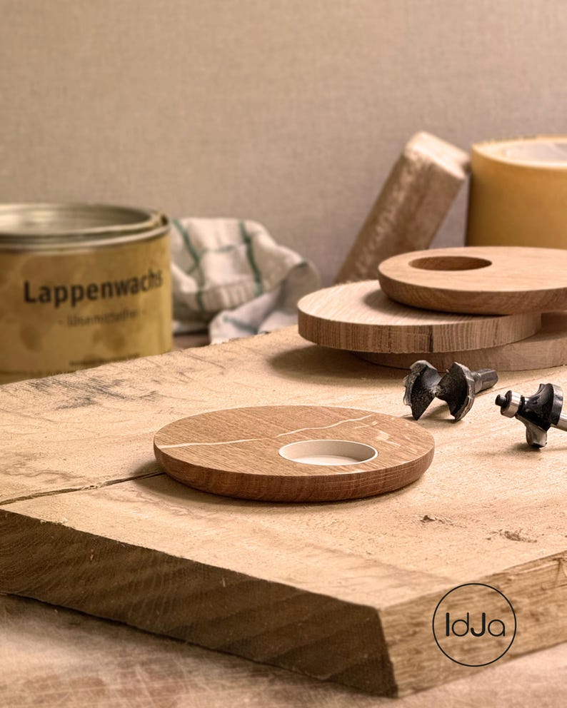 May include: A wooden candle holder with a white inlay and a circular opening. Several other wooden discs and tools are arranged on a wooden surface. A can of Lappenwachs is visible in the background.
