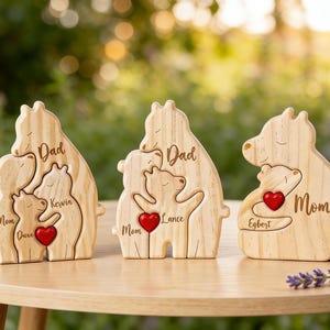 Op de afbeelding: Drie houten berenfamiliefiguren met gegraveerde namen en een rood hart. Elke berenfamilie bestaat uit een vader, een moeder en een kind. De namen zijn op de beren gegraveerd. De figuren staan op een houten tafel.