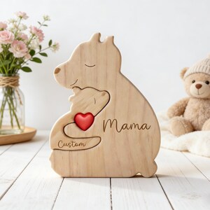 Op de afbeelding: Houten beer-vormige decoratie met een kleinere beer uitsparing, een rood hart en het woord "Mama" in cursief. Het woord "Custom" is ook gegraveerd. Een teddybeer en bloemen staan op de achtergrond.