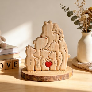 Op de afbeelding: Een houten puzzel van een berenfamilie met namen gegraveerd op elke beer. Een rood hart staat in het midden. De puzzel staat op een houten voet. Een knuffelkonijn en blokken met "LOVE" staan in de buurt.