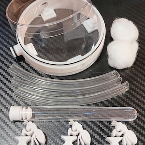 May include: A white and clear ant farm kit with a circular habitat, clear tubes, a test tube, cotton, and three white ant-shaped figurines with the text "ANTFORCE". The kit is designed for ant observation and care.