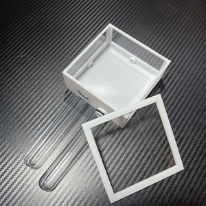 May include: A white, rectangular terrarium with a clear lid and two clear test tubes. The terrarium has a square opening and is designed for small insects or plants. The components are made of plastic and glass.