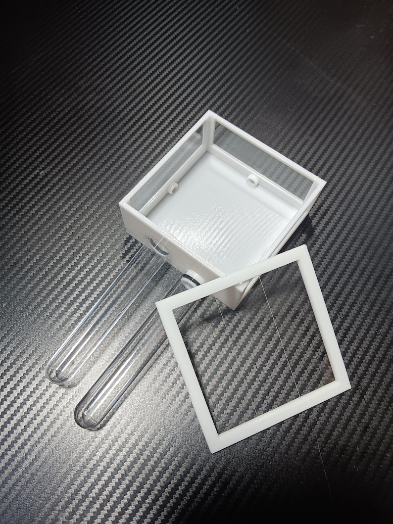 May include: A white, rectangular terrarium with a clear lid and two clear test tubes. The terrarium has a square opening and is designed for small insects or plants. The components are made of plastic and glass.