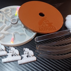 May include: An ant farm kit with a white circular base, a brown lid with the text "ANTFORGE", and several clear tubes. The kit also includes white ant-shaped figurines and cotton balls.