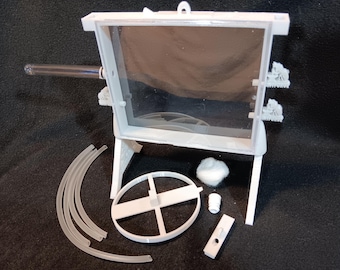May include: A white, rectangular, transparent-windowed structure with a clear tube extending from the side. Additional components include curved tubes, a circular frame, a small cylinder, and a rectangular piece, all in white.