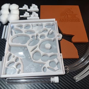 May include: An ant farm kit with various components. Includes a white and gray plastic habitat with multiple chambers, clear tubing, a pipette, cotton, and a brown piece with the text "ANTFORGE". Also includes small white figurines.