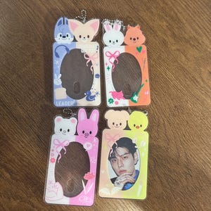 May include: Four clear plastic card holders with cartoon animal toppers. Each holder has a different design, including a blue and white one with the word "LEADER". One holder contains a photo of a person.