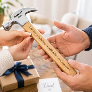 Puede incluir: Un martillo de metal plateado con mango de madera. La cabeza del martillo está marcada como Stalwart 16oz. El mango de madera presenta el texto grabado: Dad, Thanks for helping me build my life! Love, Samantha, seguido de un pequeño corazón.