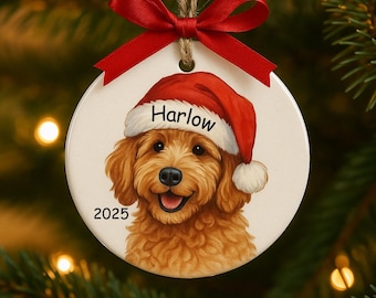 May include: Round Christmas ornament featuring a smiling golden doodle wearing a Santa hat with the name "Harlow" and the year "2025". The ornament has a red bow and string for hanging. Festive holiday decor.