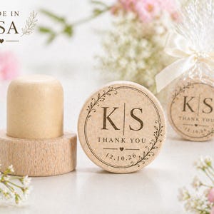 May include: A light-colored wooden bottle stopper and matching coasters. The coasters are round with the initials "KS" and the words "THANK YOU" and the date "12.10.26" printed on them. The words "MADE IN USA" are also visible.