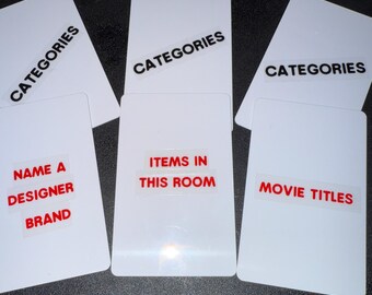 May include: White rectangular cards with text labels. The labels include "CATEGORIES", "NAME A DESIGNER BRAND", "ITEMS IN THIS ROOM", and "MOVIE TITLES". The cards are arranged on a dark surface.