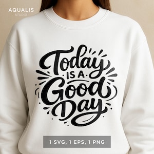 May include: White sweatshirt with the text "Today is a Good Day" in a black, cursive font. The design includes decorative flourishes and the words "1 SVG, 1 EPS, 1 PNG" at the bottom. The brand name "AQUALIS STUDIO" is at the top left.