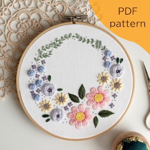以下が含まれることがあります： 白い布に花の模様が施された刺繍枠。ピンク、黄色、青の花、緑の葉、緑のつるが含まれています。「PDF pattern」の文字が右上に見えます。