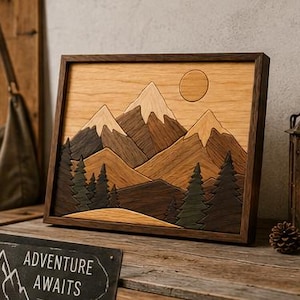 May include: A rectangular wooden wall art piece featuring a layered mountain landscape with snow-capped peaks, a circular sun, and dark green pine trees. The artwork is enclosed in a dark wood frame, showcasing various wood grain textures and tones.