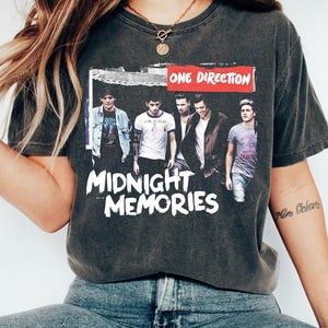 Może przedstawiać: Biały ceramiczny kubek z czarnym uchwytem i napisem "But First, Coffee" czarną, pogrubioną czcionką. Kubek stoi na białej powierzchni.