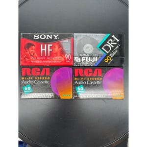Könnte beinhalten: Vier Audiokassetten. Zwei RCA Hi-Fi Stereo Audiokassetten mit 60 Minuten Kapazität. Eine Sony HF 90-Minuten-Kassette und eine Fuji DR-I 90-Minuten-Kassette. Die Kassetten befinden sich in ihrer Originalverpackung.