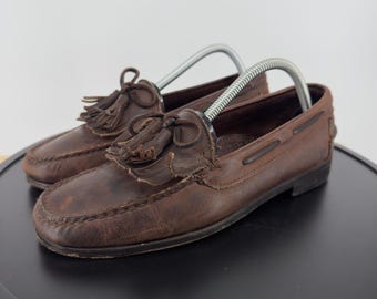 Mocasines Cole Haan Country para hombre, de piel marrón, con borlas y tejido kilt, confeccionados con Memory Flex y cosidos a mano.