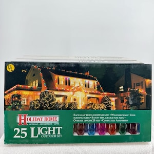 Pode incluir: Uma caixa de conjunto exterior Holiday Home de 25 luzes. A caixa apresenta uma cena noturna de uma casa decorada com luzes de Natal. A caixa inclui uma fileira de lâmpadas coloridas. O texto na caixa diz: "Cada lâmpada queima de forma independente, à prova de intempéries, lâmpadas frias, fusível substituível, comprimento total 7,62 metros, totalmente montado."