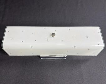 Può includere: Una copertura rettangolare per lampada in vetro smerigliato bianco con un motivo sparso di piccole stelle nere a quattro punte. La copertura ha una forma liscia e allungata con un singolo pomello circolare centrale color argento.