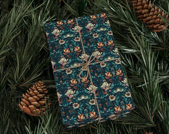 Könnte beinhalten: Ein rechteckiges Geschenk, verpackt in gemustertem Papier mit einem tealfarbenen Hintergrund und einem floralen Design in Orange und Creme. Das Geschenk ist mit Bindfaden gebunden und liegt auf Kiefernnadeln.