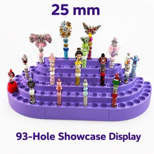 May include: A purple 93-hole showcase display stand with 25 mm diameter openings, featuring an array of decorative beaded pens arranged in tiers. The pens are adorned with various colorful charms, including bows, cartoon characters, and rhinestones.