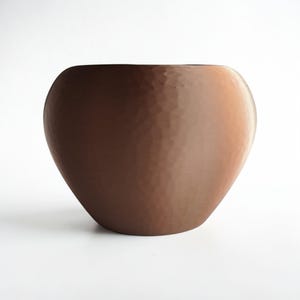 May include: A brown, hammered-texture ceramic bowl with a wide opening and rounded shape. The bowl has a smooth, curved silhouette and a warm, earthy tone, suitable for home decor.