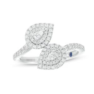 Puede incluir: Un anillo de oro blanco con dos racimos de diamantes en forma de pera. Cada racimo presenta un diamante central en forma de pera rodeado por un halo de diamantes más pequeños. Una pequeña gema azul está engastada en la banda.