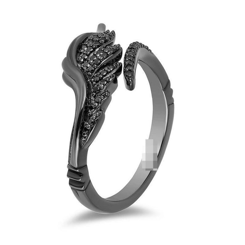 May include: A black ring with a unique design. The ring features a stylized feather or leaf shape on one side, encrusted with small black stones. The band is open, and the ring has a dark, matte finish.