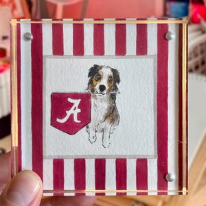 Peut inclure: Sous-verre carr&eacute; en acrylique avec une peinture &agrave; l'aquarelle d'un chien tenant une banni&egrave;re avec un "A" rouge sur fond blanc. Le dessous de verre a une bordure ray&eacute;e rouge et blanche et une bordure dor&eacute;e.