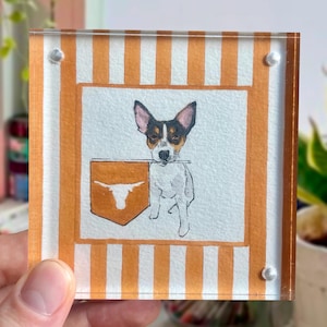 Peut inclure: Bloc acrylique carr&eacute; avec une illustration &agrave; l'aquarelle d'un chien tenant une banni&egrave;re avec un symbole de longhorn. Le bloc a des bordures ray&eacute;es orange et blanches. Le bloc est tenu dans une main.