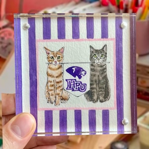 Peut inclure: Sous-verre carr&eacute; en acrylique avec deux illustrations de chats &agrave; l'aquarelle. L'un est tigr&eacute;, l'autre gris. Ils encadrent une banni&egrave;re violette et blanche avec les lettres "HPU" et un logo de panth&egrave;re. Le dessous de verre a une bordure ray&eacute;e.