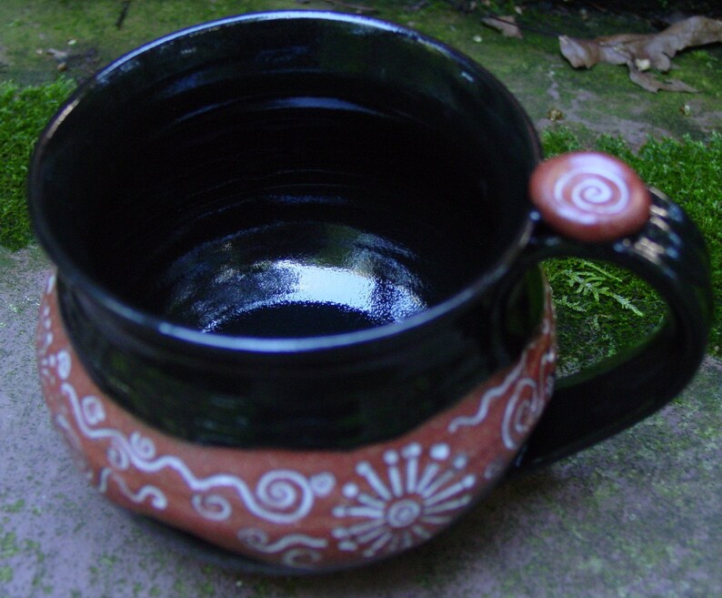 May include: A black ceramic mug with a brown rim and white swirl designs. The mug has a handle with a brown knob.