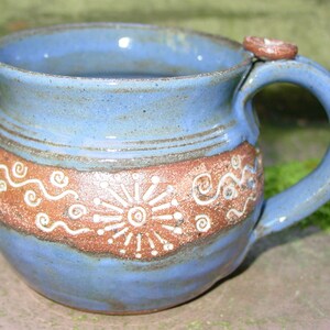 May include: A blue and brown ceramic mug with a white design. The mug has a rounded body and a handle.