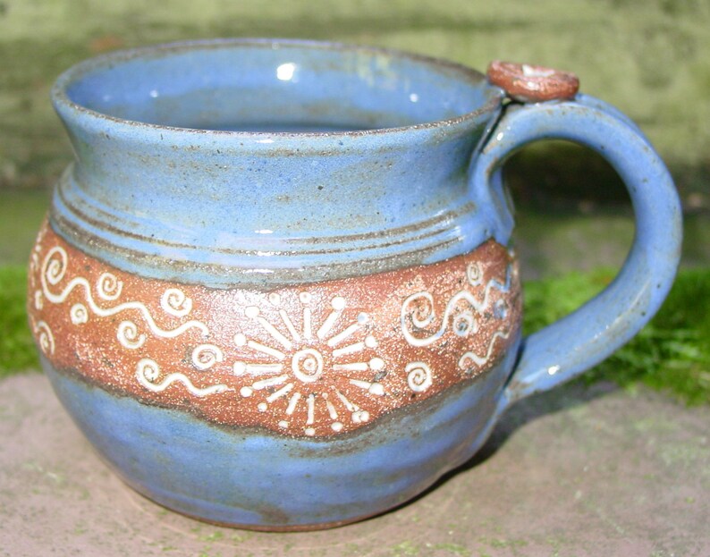 May include: A blue and brown ceramic mug with a white design. The mug has a rounded body and a handle.