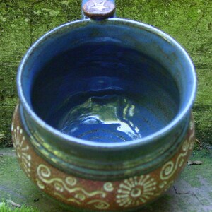 May include: A blue and brown ceramic mug with a star-shaped handle. The mug has a white glaze with brown and white swirls and designs.