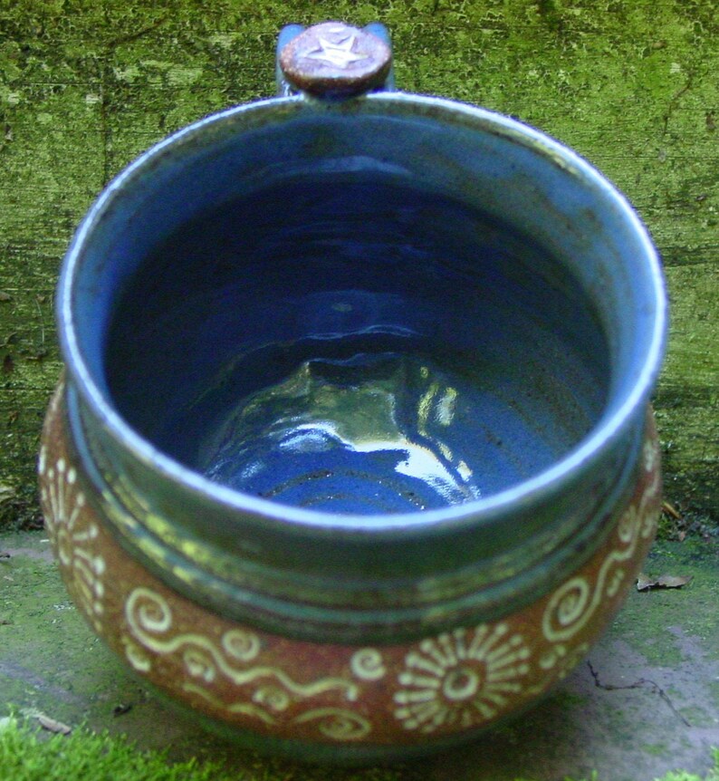 May include: A blue and brown ceramic mug with a star-shaped handle. The mug has a white glaze with brown and white swirls and designs.