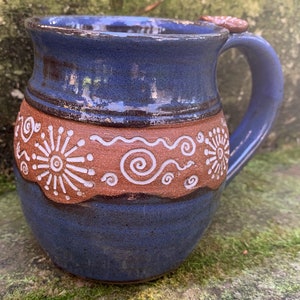 May include: A blue ceramic mug with a brown band and white swirl designs. The mug has a rounded body and a handle.