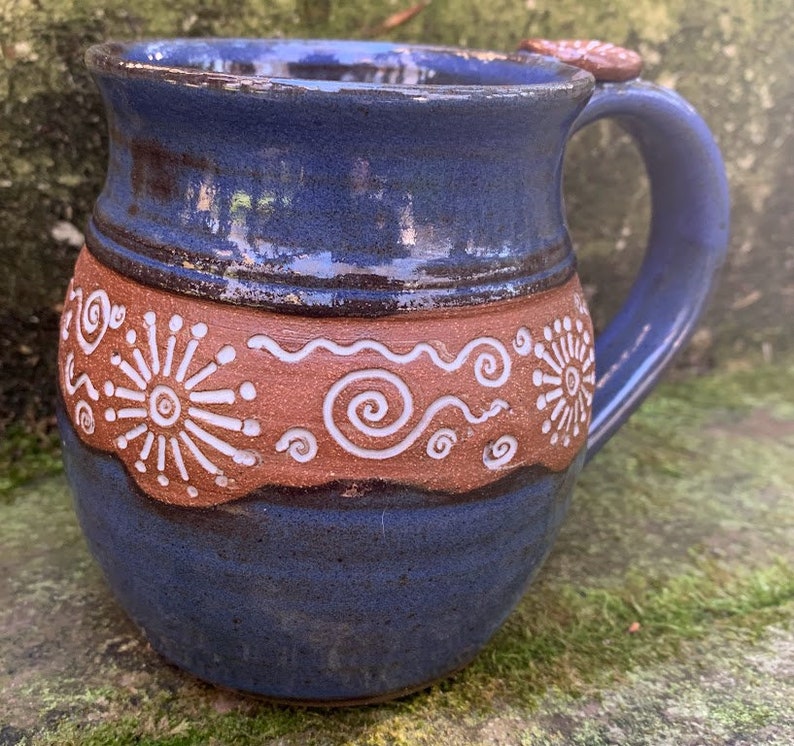 May include: A blue ceramic mug with a brown band and white swirl designs. The mug has a rounded body and a handle.