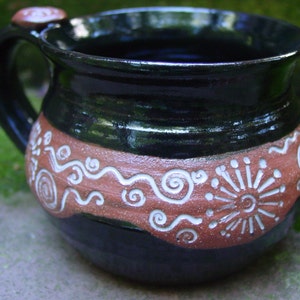 May include: A black ceramic mug with a brown band and white swirl designs. The mug has a rounded shape and a handle.