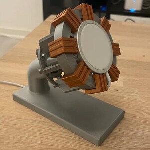 Può includere: Un supporto di ricarica grigio e marrone stampato in 3D per un caricatore wireless. Il supporto ha una base rettangolare, un braccio curvo e un supporto circolare con una superficie di ricarica bianca. Il supporto ha dettagli marroni.