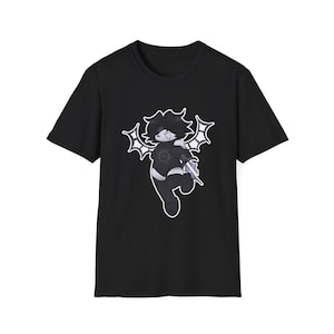 Puede incluir: Camiseta negra con un diseño de personaje de dibujos animados. El personaje tiene pelo oscuro, alas y un arma. El gráfico está delineado en blanco, contrastando con la tela negra. El diseño es una ilustración única.