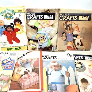 May include: A collection of eight vintage sewing patterns for making doll clothes and accessories. The patterns feature a variety of designs, including a Cabbage Patch Kids outfit, a teddy bear, and a doll crib. The patterns are all in good condition and would be a great addition to any doll collector's collection.