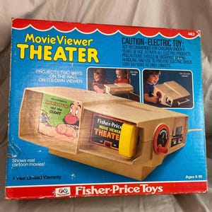 May include: A vintage Fisher-Price Movie Viewer Theater toy in a blue and red cardboard box. The box features text including Movie Viewer THEATER, Fisher-Price Toys, and product details. The toy is tan with a yellow knob and red dial.